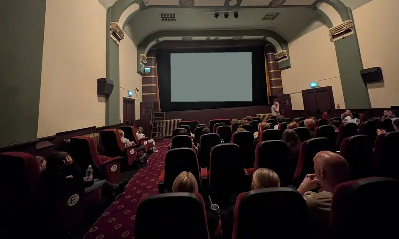 Rows of red seats in a small cinema, the audience seen from behind, facing a blank screen
